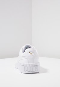 Zapatilla blanca de cuero con una superficie texturada, que presenta un logotipo dorado de Puma y una suela blanca gruesa con la inscripción "PUMA".