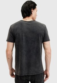 Dunkelgraues Baumwoll-T-Shirt mit lockerer Passform, kurzen Ärmeln, rundem Halsausschnitt und subtilem, abgenutztem Look. Rückansicht, die die Schlichtheit des Designs zeigt.