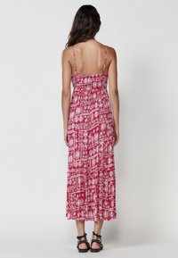 Rotes Maxikleid mit weißen Tribal-Mustern, verstellbaren Spaghettiträgern und einem gerüschten Rücken, mit einem gestuften Saum und schwingendem Stoff.