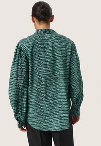 Groen gemusterde shirt met een losse pasvorm en lange mouwen, voorzien van een ruitpatroon in zwart en teal, gemaakt van lichtgewicht stof.