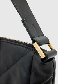 Fekete bőr kézitáska steppelt textúrával, aranyszínű fém díszítéssel és cipzáras záródással. Láthatóak a sima fogantyú részletei.