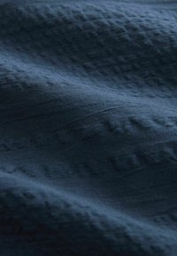 Mörkblå texturerad tyg med subtila mönster, som har en mjuk, slät kvalitet och varierande ytdimensioner.