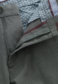 Grå tekstureret stof med et subtilt mønster, udstyret med en lynlås og maroon accenter. Foret med et blåt geometrisk print.