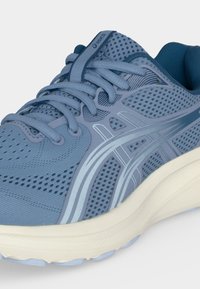 Μπλε αθλητικό παπούτσι Asics με πλέγμα στο πάνω μέρος, συνθετικές ενισχύσεις, μαλακή λευκή σόλα και κορδόνια μπροστά.