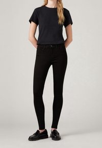 Svarta smala jeans med en slät textur, femficksdesign och hög midja, tillsammans med en åtsittande svart t-shirt och svarta loafers.