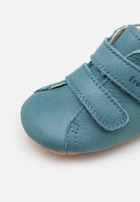 Blaues Lederschuhwerk mit abgerundetem Zehenbereich, zwei verstellbaren Klettverschlüssen und kontrastierenden Nähten. Weiche Sohle für Komfort und Flexibilität.