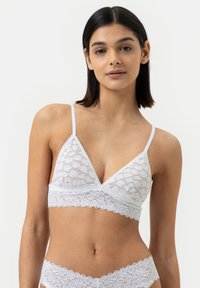 Witte kanten bralette met een driehoekige vorm, verstelbare bandjes, geschulpte rand en zachte textuur met bloemenpatronen.
