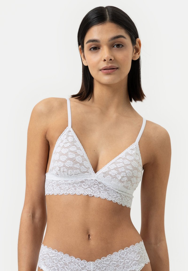 Witte kanten bralette met een driehoekige vorm, verstelbare bandjes, geschulpte rand en zachte textuur met bloemenpatronen.