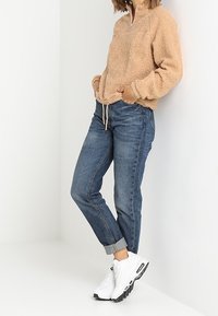 Polaire beige à col zippé quart, ourlet et poignets élastiques, portée avec un jean bleu clair retroussé et des baskets blanches.