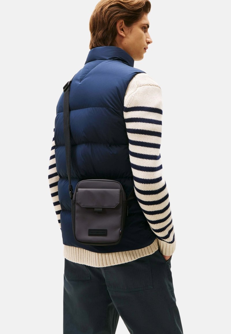 Chaleco de plumas navy, suéter de punto crema con rayas navy y bolso de bandolera. El bolso es gris con cierre de solapa y superficie texturizada.