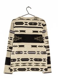 Beige Pullover mit langen Ärmeln und schwarzen sowie grauen geometrischen und tribalartigen Mustern, der an einem schwarzen Kleiderbügel vor einem weißen Hintergrund hängt.