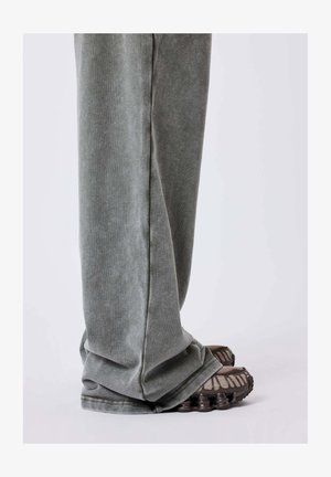 Pantalones de chándal grises con una textura suave y un diseño ajustado, combinados con zapatillas deportivas marrones que presentan un patrón de suela distintivo.