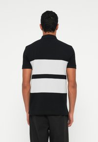 Black and grey polo shirt featuring horizontal stripes, textured knit fabric, a collared neckline, and short sleeves.