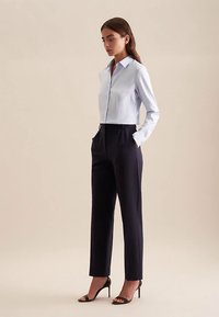 Lichtblauw cropped overhemd met kraag, gecombineerd met zwarte hoge taille broek en zwarte hoge hak sandalen, tegen een neutrale achtergrond.