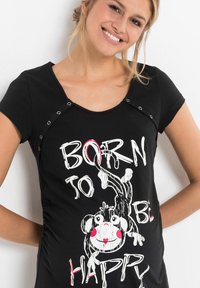 T-shirt di cotone nero con maniche corte, caratterizzato da un design grafico di una scimmia e il testo "NATO PER ESSERE FELICE" in bianco e rosso. Dettagli a scatto sul colletto.