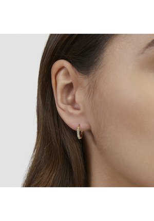 Nahaufnahme eines Frauenohres mit glattem braunem Haar, das einen kleinen goldenen Creolenohrring mit Perlenbesatz trägt.