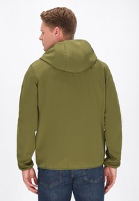 Svetlozelená bunda s kapucňou, dĺžky po kolená, vyrobená z hladkej tkaniny. Má elastické manžety, predný zips a voľný strih, nosená nad modrými džínsami.