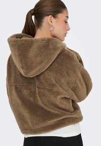 Bruine fleece hoodie met een zachte textuur, een vaste capuchon en een ontspannen pasvorm. Voorzien van een zichtbare naadontwerp en een vlakke zoom.