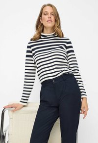 Langarmig gestreept shirt in marineblauw en wit met een hoge hals, gecombineerd met donkere, op maat gemaakte broeken. Soepele stof, reguliere pasvorm.