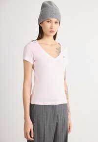 Φωτεινό ροζ κοντομάνικο μπλουζάκι V με εφαρμοστή γραμμή, κατασκευασμένο από μαλακό βαμβάκι. Ριχτό γκρι σκουφάκι με μικρό λογότυπο. Κομψή απαλότητα υφής, κοντά μανίκια.