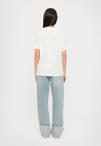 T-shirt blanc à manches courtes avec un design simple, associé à un jean large bleu clair avec un ourlet replié.