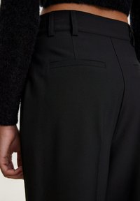 Schwarze maßgeschneiderte Hosen aus glattem Stoff, mit zwei Gesäßtaschen und hoher Taille, detaillierten Nähten und schmaler Passform.