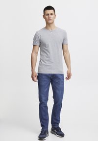 Camiseta gris de manga corta con cuello en V, combinada con jeans azules con detalles de costura en los bolsillos traseros y zapatillas negras con acentos grises.