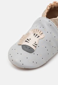 Graue Lederpantoffel mit gepunktetem Muster; zeigt eine Applikation eines Zebra-Gesichts in Creme und Schwarz, akzentuiert mit einer strukturierten Mähne.