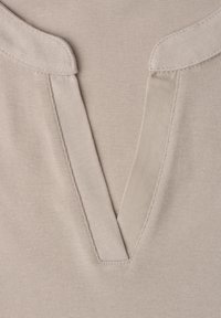 Encolure de chemise beige à col, ouverture en V et coutures visibles sur tissu doux.