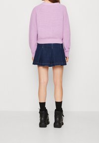 Pull en lilas tricoté avec un ourlet côtelé, associé à une jupe plissée en denim foncé. Des bottines noires et des chaussettes complètent l'ensemble.