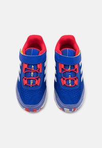 Blue athletic shoes with red accents, mesh upper, padded collar, Velcro strap, rubber sole, and white stripes on the sides.