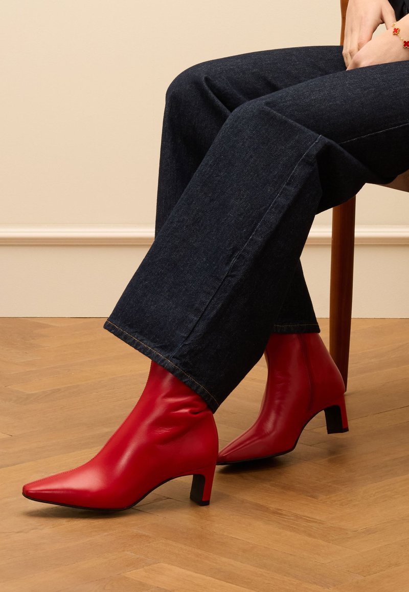 Rote Leder-Ankle-Boots mit spitzem Kopf und mittelhohem Blockabsatz, kombiniert mit weit geschnittenen Jeans in Dunkelblau. Glatte Textur.