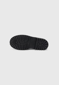Talpa de pantof din cauciuc negru cu un model deaderă rugged, incluzând canale dreptunghiulare și în formă de cruce, prezentată pe un fundal alb.
