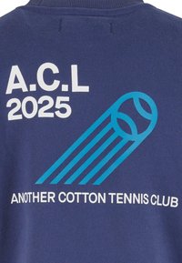 Námornícky bavlnený sveter s bielym textom "A.C.L 2025" a "ANOTHER COTTON TENNIS CLUB" s modrou grafikou tenisových loptičiek a pohybovými čiarami.