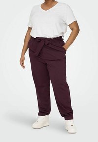 White V-neck t-shirt paired with high-waisted maroon pants featuring a tied belt. Model wears white sneakers. Smooth fabric and relaxed fit.