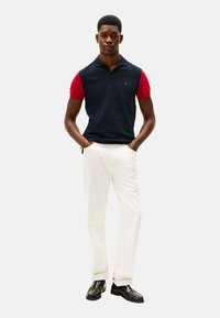 Polo de manga corta azul marino y rojo con cuello, combinado con jeans blancos y mocasines de cuero negros. Diseño de atuendo simple y clásico.