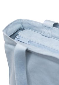 Ljust blå tygväska med dragkedjetopp och robusta handtag. Insidan har ett strukturert foder och en liten märkestagg.