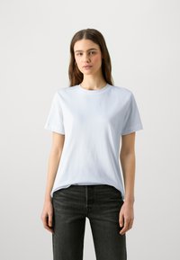 Camiseta de algodón azul claro con cuello redondo y mangas cortas, combinada con jeans negros. Textura suave, sin patrones ni gráficos visibles.