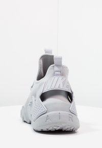 Nike-sneaker i ljusgrått med mesh och gummiaccents, försedd med dragflik, synlig varumärkestext och texturerad sula för grepp.