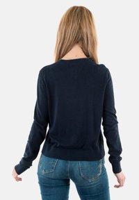 Maglione a maglia di un blu navy scuro con scollatura rotonda e polsini a coste, abbinato a jeans blu con tasche posteriori e dettagli di cucitura discreti.