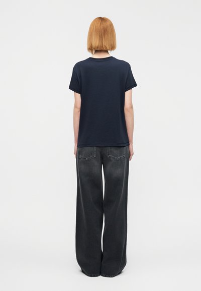 Μπλε ναυτικό t-shirt από βαμβάκι, με στρογγυλή λαιμόκοψη και κοντά μανίκια, σε συνδυασμό με ψηλόμεσα μαύρα παντελόνια φαρδιάς γραμμής με πίσω τσέπες.