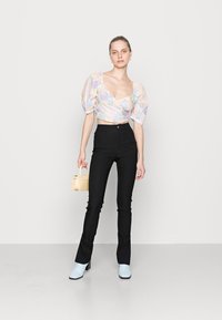 Top cropped de mangas bufantes em padrão floral pastel, combinado com calças pretas de cintura alta. Apresenta botas azul claro e uma pequena mala bege.