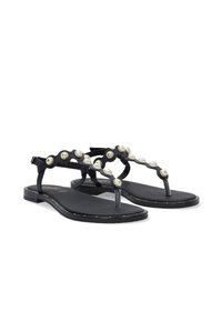 Sorte flade sandaler med en tætsiddende design, udstyret med en dekorativ bølget rem prydet med metalliske muslingelignende detaljer. Blød sål og minimal syning.