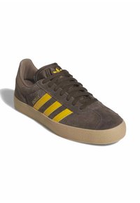 Sneaker in suede marrone con strisce gialle e marroni, punta rotonda e suola in gomma testurizzata. Presenta lacci e un piccolo logo sulla linguetta.