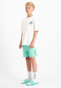 Witte T-shirt met grafisch ontwerp, mintgroene shorts met zijzakken en merknaam, witte sokken en mintgroene slides. Eenvoudige, casual stijl.