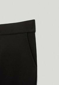 Pantalon noir à taille repliée avec poche latérale visible sur un fond clair.