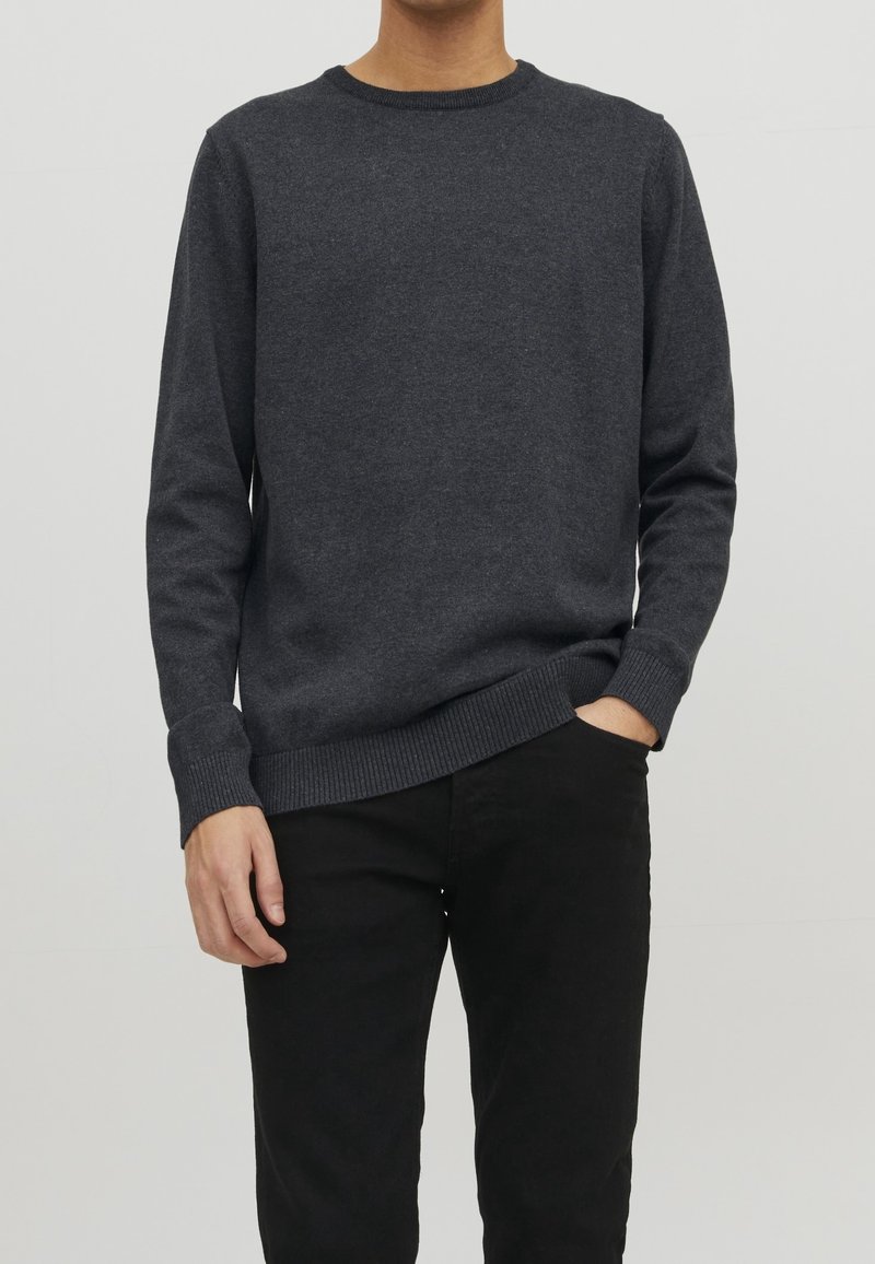 Grauer Rundhalspullover aus Strickstoff mit langen Ärmeln und gerippten Bündchen und Saum. Getragen mit schwarzen Hosen. Angenehme Textur.