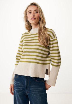 Stribet striktrøje i creme og olivengrøn, høj halsudskæring, ribbet struktur, sideslids, parret med mørkeblå jeans.