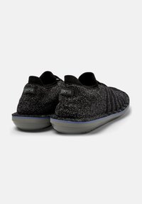 Black knitted slip-on shoes featuring a textured design, gray rubber sole, and a small logo tag on the heel.