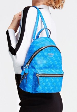 Mochila sintética azul de forma redondeada, con el patrón del logo 'Guess', herrajes plateados y un bolsillo delantero con cremallera.